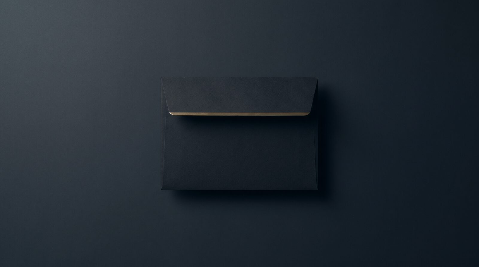 A dark unsealed envelope lying flat, a thin line of brass at its edge