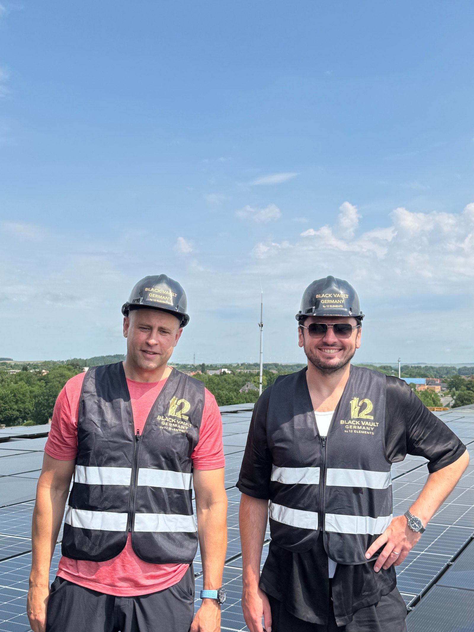 Lars Gottschligg und Denys Tsvaig mit BLACK VAULT GERMANY Helmen und 12-Elements-Westen auf dem Dach des Kubus, dahinter das Photovoltaikfeld bis zur Attika